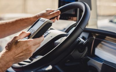 A driver with one hand on the steering wheel, the other on a remote