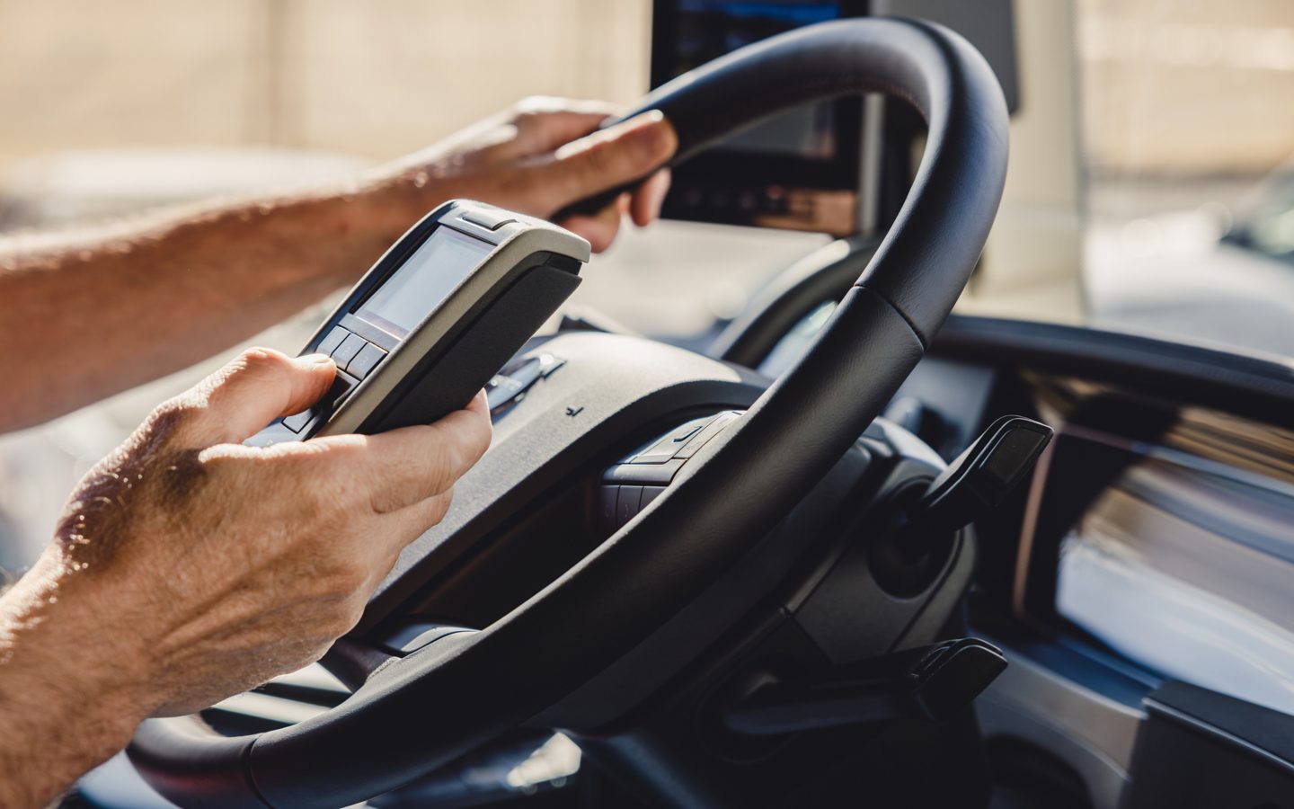 A driver with one hand on the steering wheel, the other on a remote