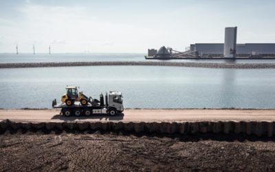 A Volvo FMX truck, laden with cargo, navigates its way along the water's edge