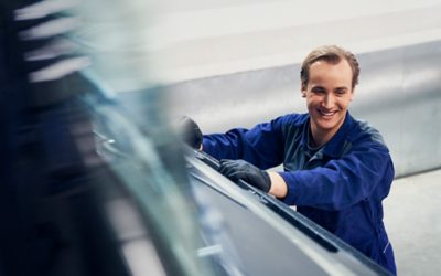 Een glimlachende man met blauwe kleren aan, en die naast een vrachtwagen staat