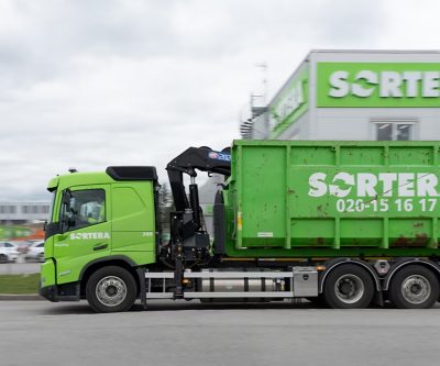 Volvo kamion s kontejnerom za reciklažu prolazi kroz industrijsku zonu, namijenjen za transport otpada i materijala za reciklažu.