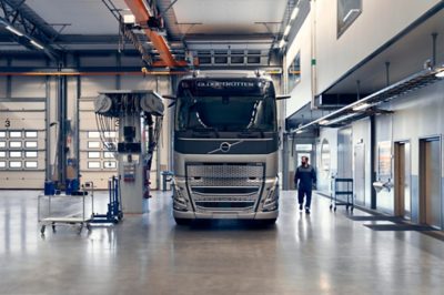 Samochód ciężarowy Volvo zaparkowany w nowoczesnym warsztacie serwisowym, obok którego stoi technik, a w hali znajduje się sprzęt serwisowy.
