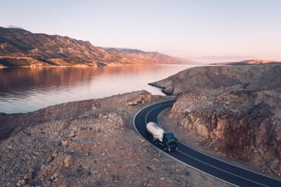 Ciężarówka Volvo FM jedzie krętą, nadmorską drogą górską o zachodzie słońca.