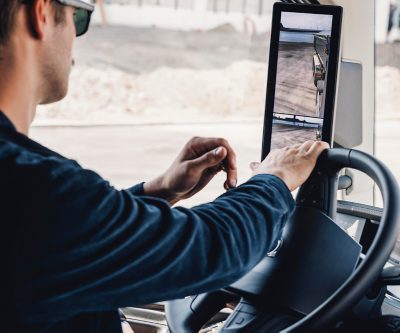 Close-up van een chauffeur die een digitaal beeldscherm in de zijspiegel in de cabine van een Volvo-vrachtwagen bedient, waarmee hij via een camera het zicht naar achteren kan bekijken.