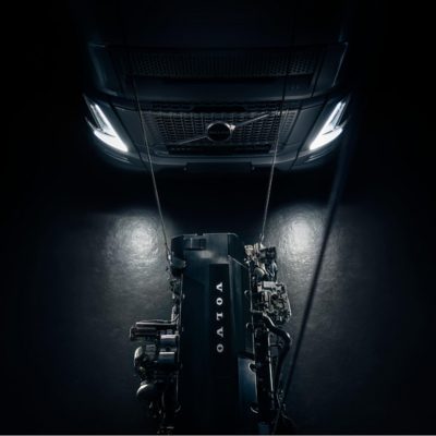 Vista frontale di un camion Volvo sopra un motore sospeso in uno studio buio, mostrata in una sequenza che evidenzia il collegamento tra veicolo e gruppo propulsore.