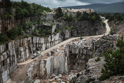 Nákladné vozidlo Volvo naložené štrkom stojí na širokej štrkovej ploche vedľa žltého kolesového nakladača Volvo v oblasti podobnej kameňolomu s veľkými hromadami kameňov.