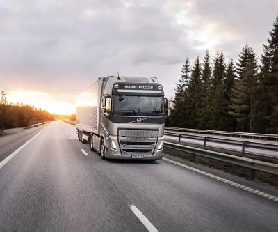 Een Volvo-vrachtwagen rijdt over een snelweg bij zonsondergang, met een bos langs de weg, en legt het langeafstandstransport vast in het warme avondlicht.