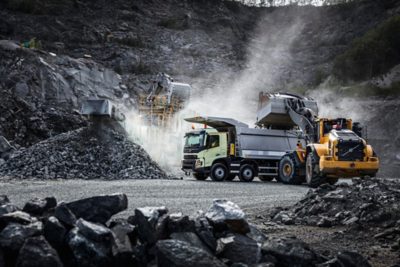 Samochód ciężarowy Volvo zaparkowany w kamieniołomie, podczas gdy ładowarka kołowa Volvo opróżnia łyżkę z kamieniami do skrzyni ładunkowej.