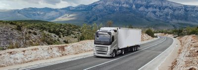 Een Volvo-vrachtwagen rijdt over een bochtige weg door een bergachtig landschap, met weidse uitzichten en ruig terrein op de achtergrond.