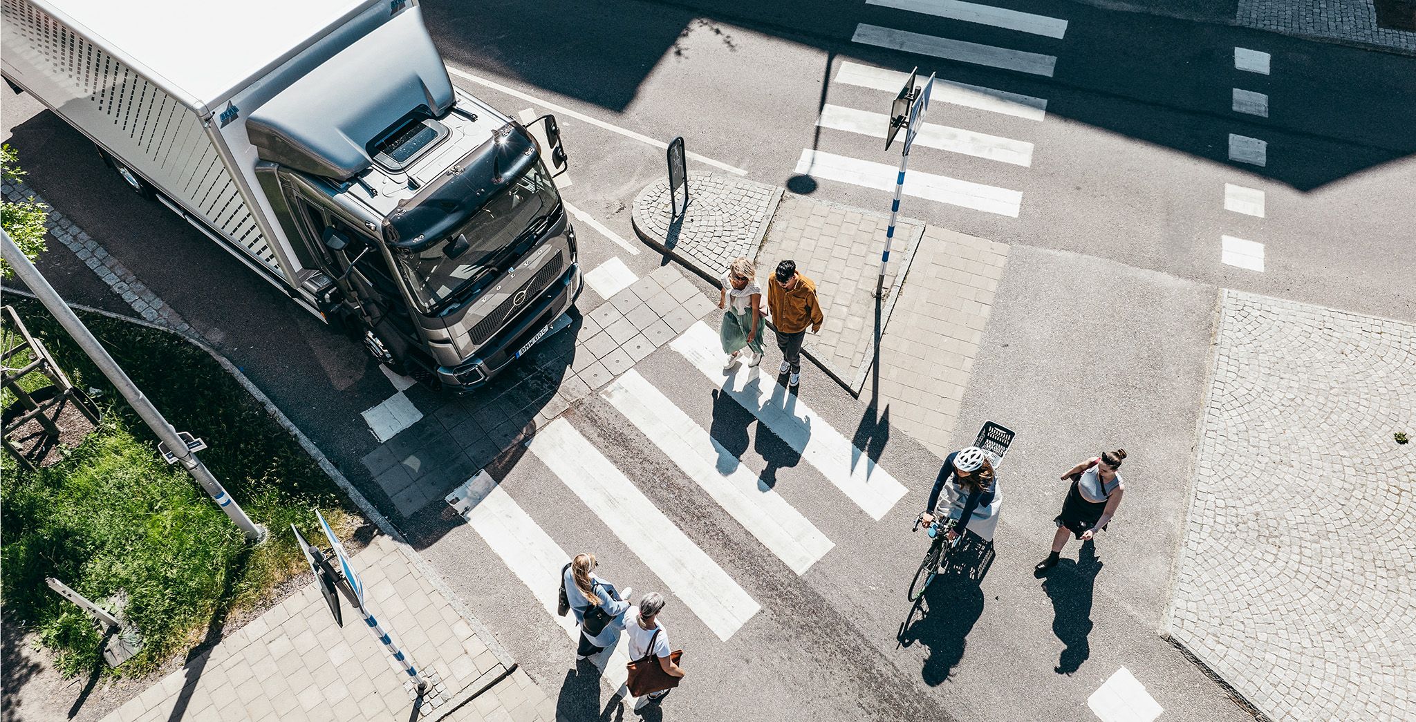 俯視圖：一輛 Volvo 貨車在市區行人穿越道前停下，讓行人安全通行。