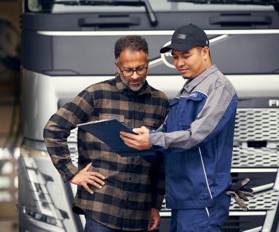 Dois homens a rever documentos numa prancheta em frente a um camião Volvo, a discutir pormenores de serviço ou manutenção.