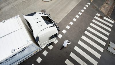 Draufsicht auf einen Radfahrer, der an einem Zebrastreifen vor einem abbiegenden LKW eine Straße überquert, was auf Bedenken hinsichtlich der Verkehrssicherheit hinweist.