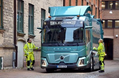 Samochód ciężarowy Volvo pracujący na wąskim dziedzińcu miejskim z dwoma członkami załogi ubranymi w odzież o wysokiej widoczności.