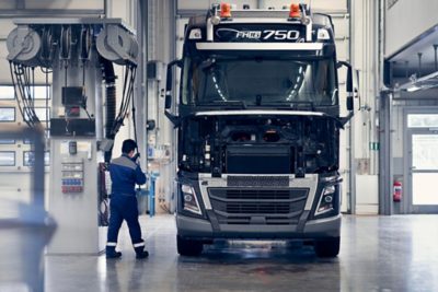 Samochód ciężarowy Volvo FH16 w jasnej stacji obsługi z otwartymi przednimi ścianami, podczas gdy w pobliżu pracuje technik.
