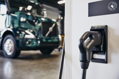 Image of a Volvo charging station in the foreground with a Volvo VNR Electric in the background out of focus