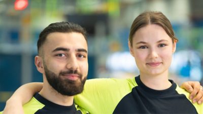 Two young employees in workwear standing together in a workshop, representing teamwork and early career development.
