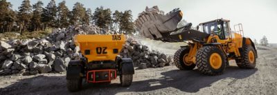  The electrical dumper, Volvo TA15, is being loaded with crushed stone from a Volvo excavator in a quarry environment.