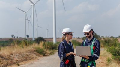 Two windpower engineers in discussion in front of an array of wind turbines.