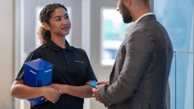 A Volvo employee carrying a spare part box while talking to a customer
