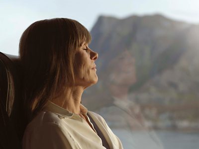 A female coach passenger with closed eyes and mountains in the background