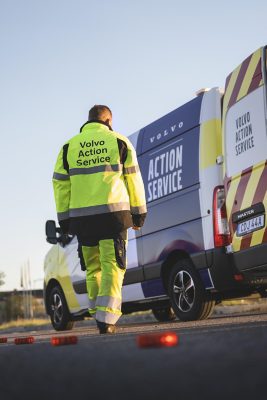 Man wearing a high visibility jacket bearing the text Volvo Action Service walking towards a truck marked with Volvo Action Service with his back turned towards the camera