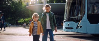 A Volvo electric bus safely stopping for two children crossing a street